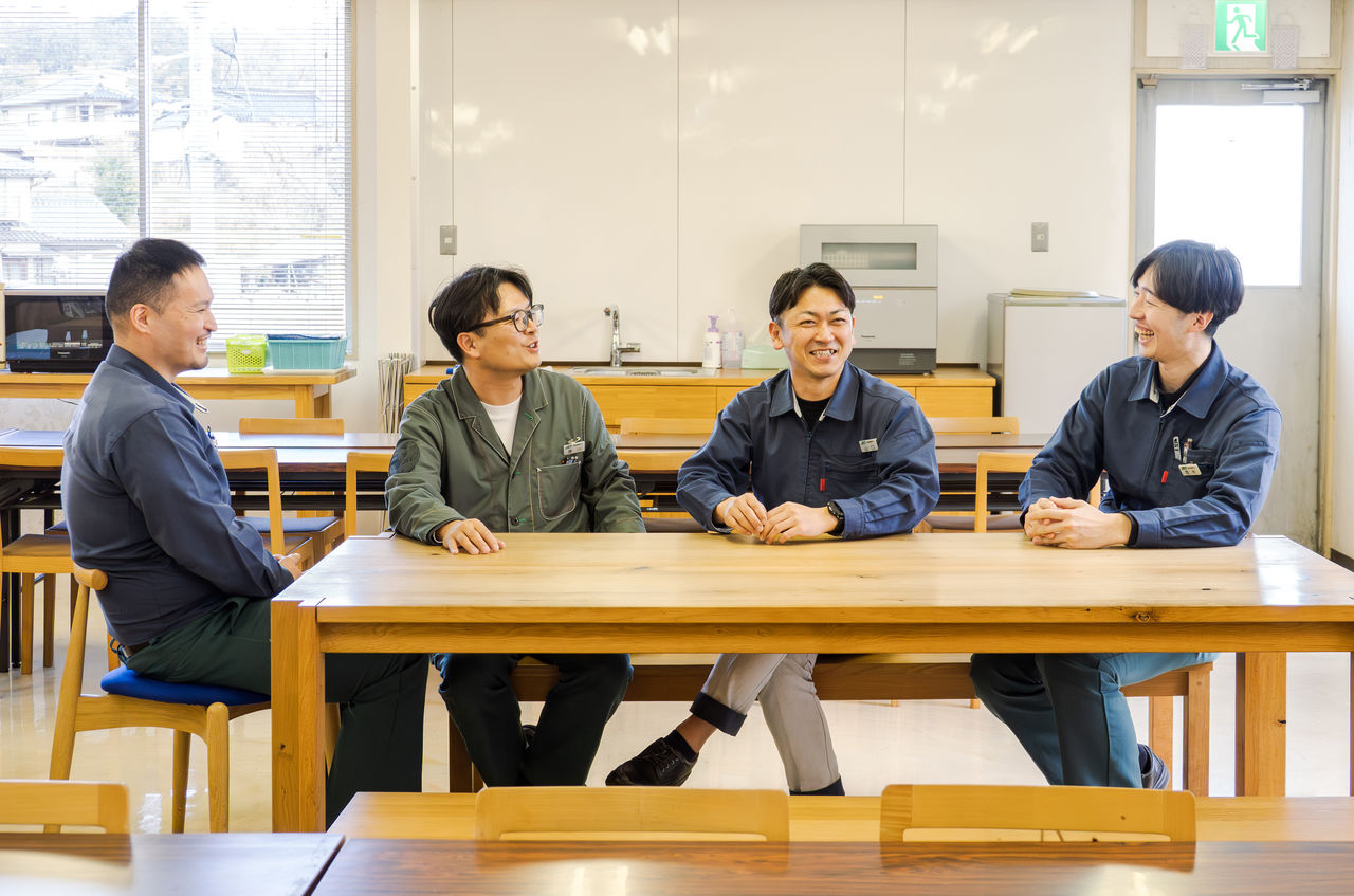 食堂のテーブルを囲み、4人の男性社員が笑顔で談笑している様子