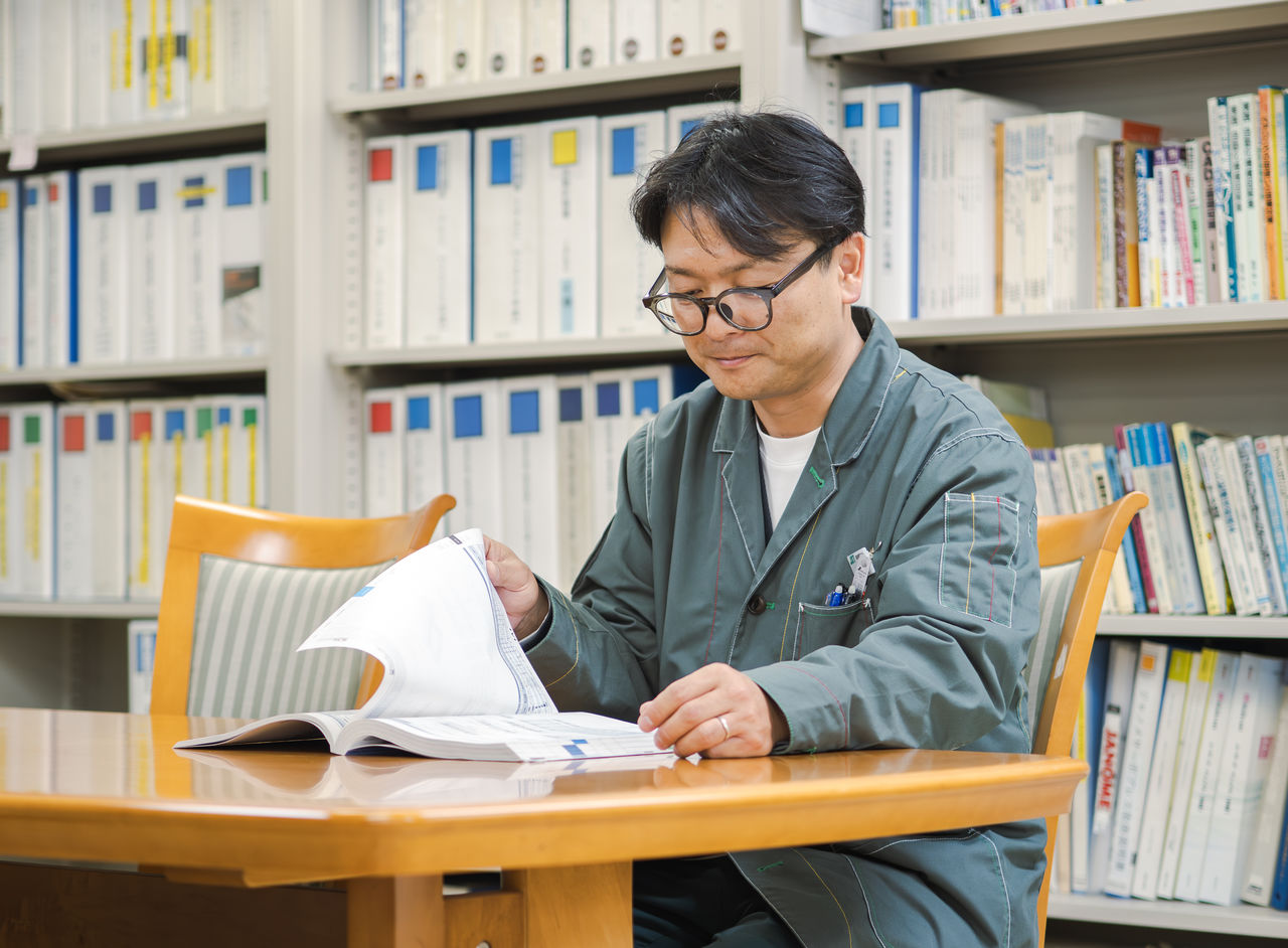 黒川さんが書棚の前のテーブルに座り、ファイルに綴じられた資料を読んでいる様子