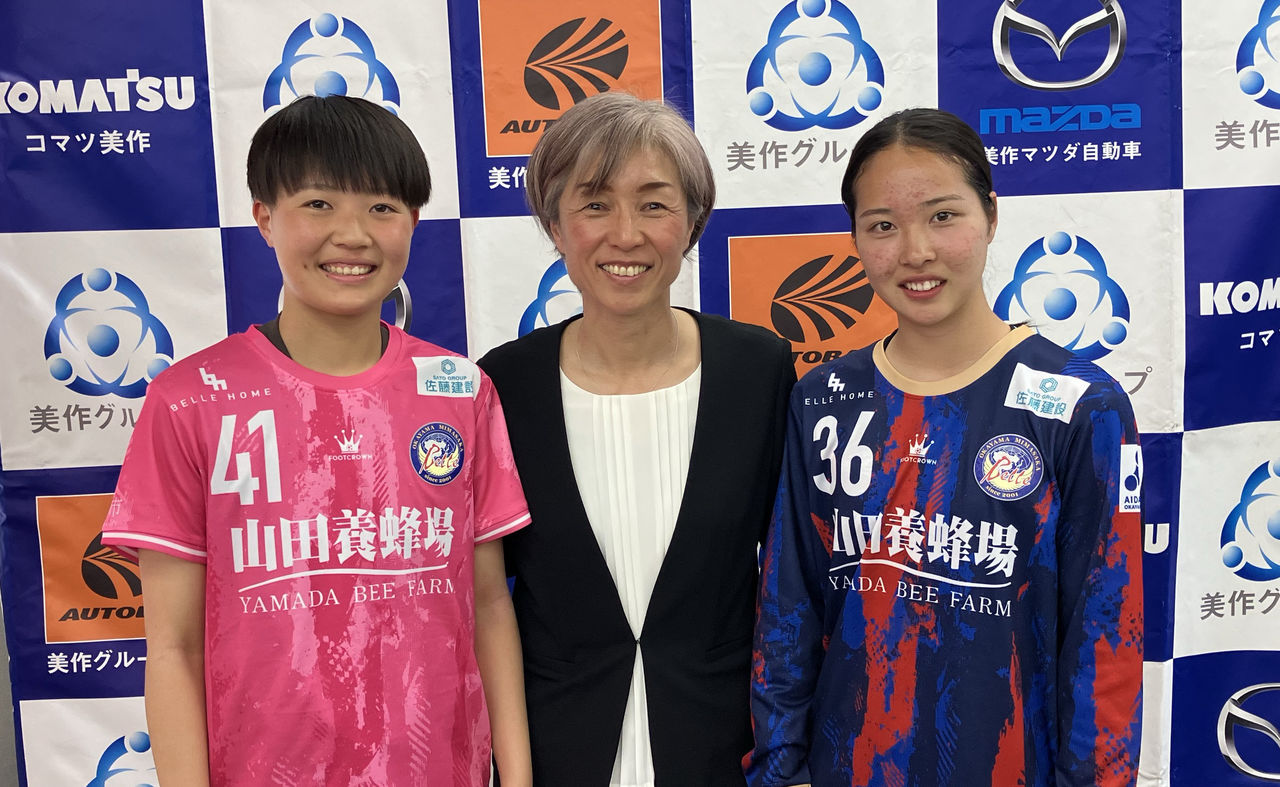 美作グループのロゴパネルを背景に撮影された、大部由美さんとユニフォーム姿の女子サッカー選手2名の写真。