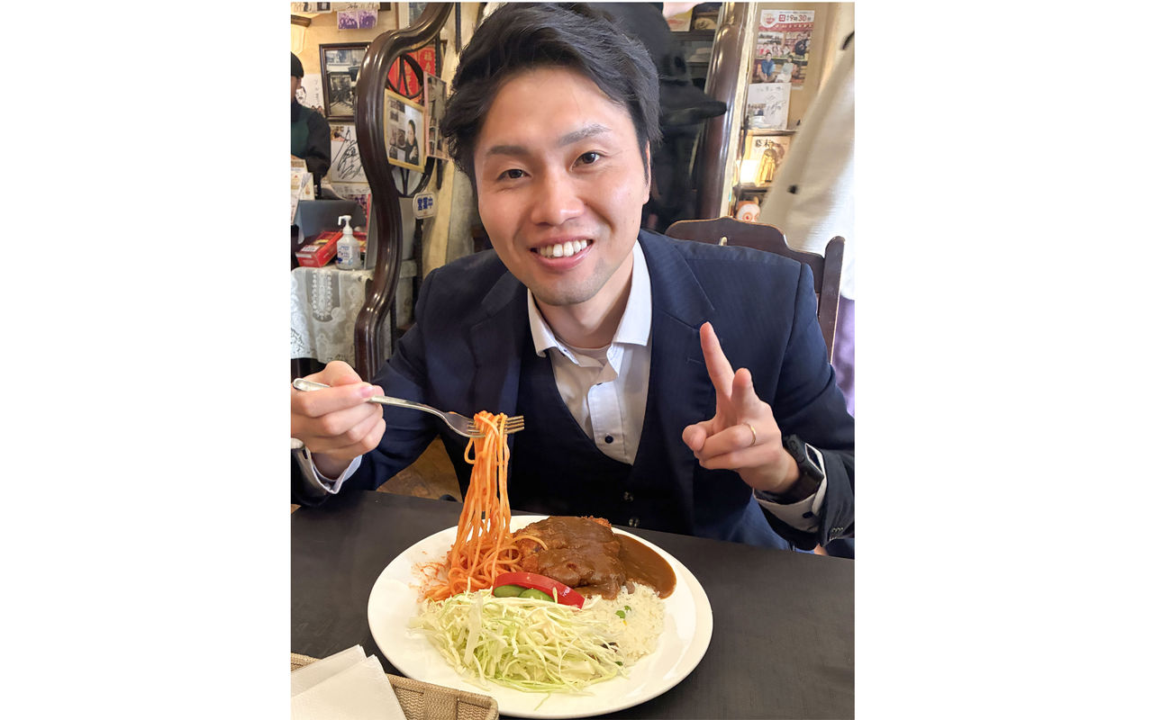 お皿に盛られたトルコライスを前にピースサインをして笑顔を見せる田口さん