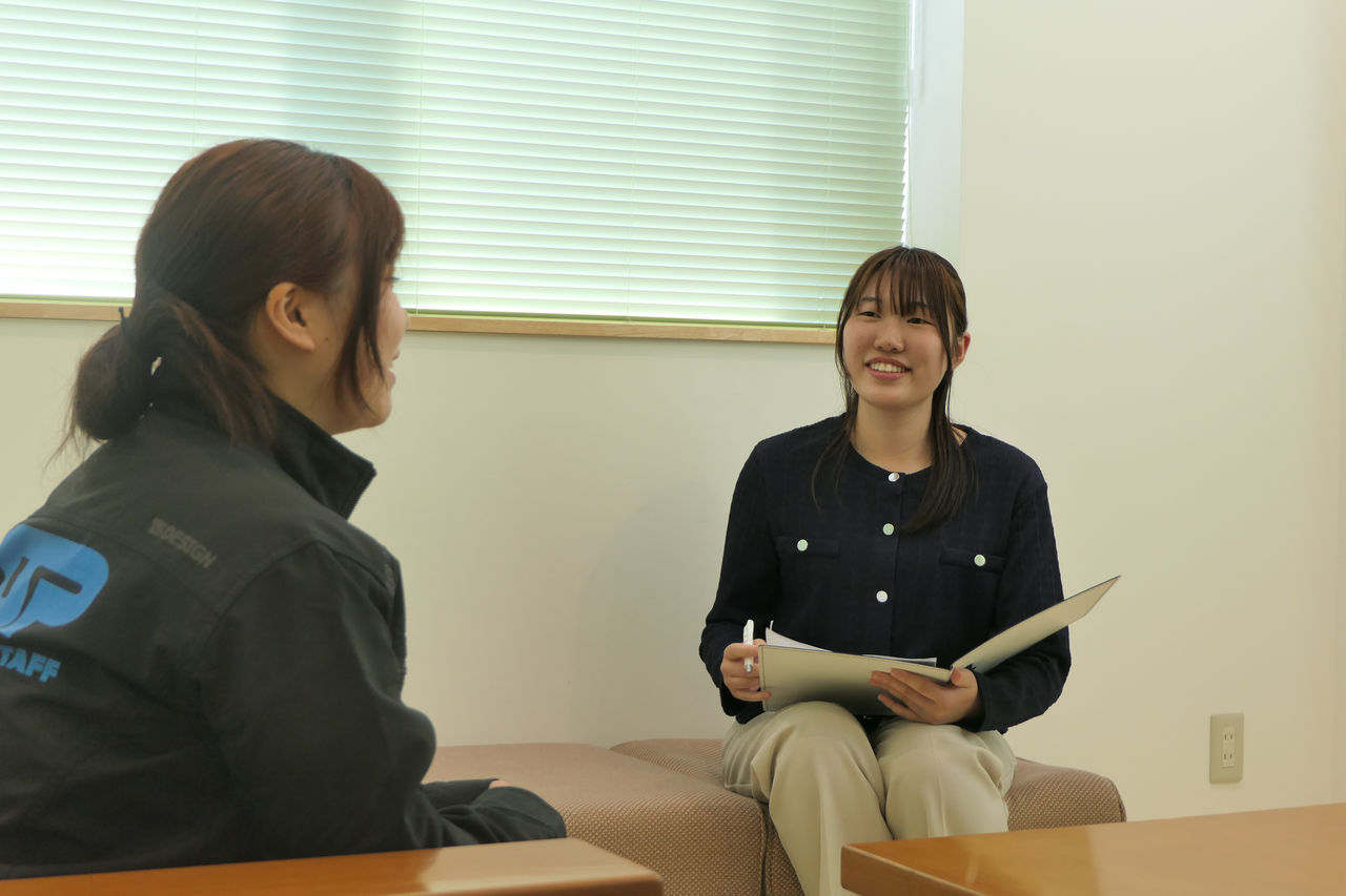 応接室のソファに座り、書類を手に持って対面に座る杉本さんへインタビューを行う磯山柚姫さんの様子。