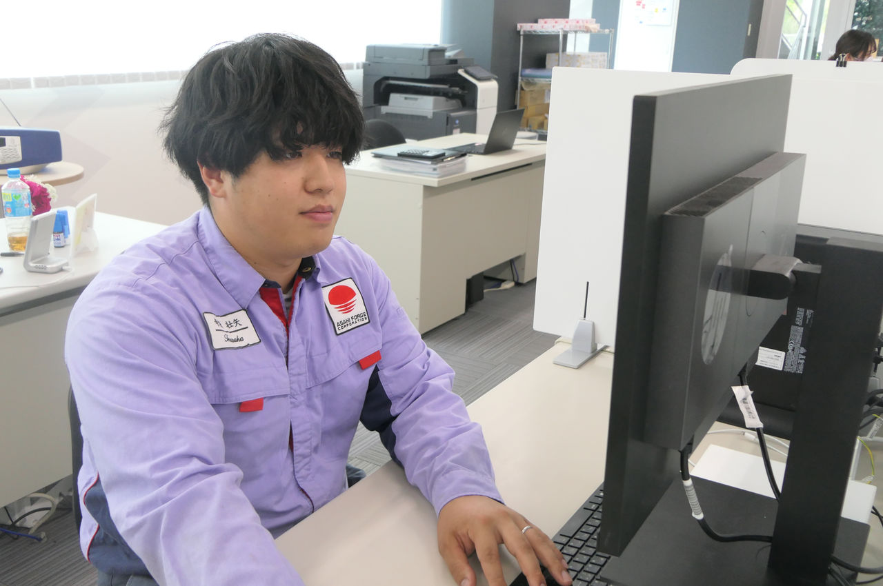 明るいオフィスのデスクに座り、パソコンのモニターを見ながらキーボードとマウスを操作して、図面や3Dモデルの作成業務を行っている様子。