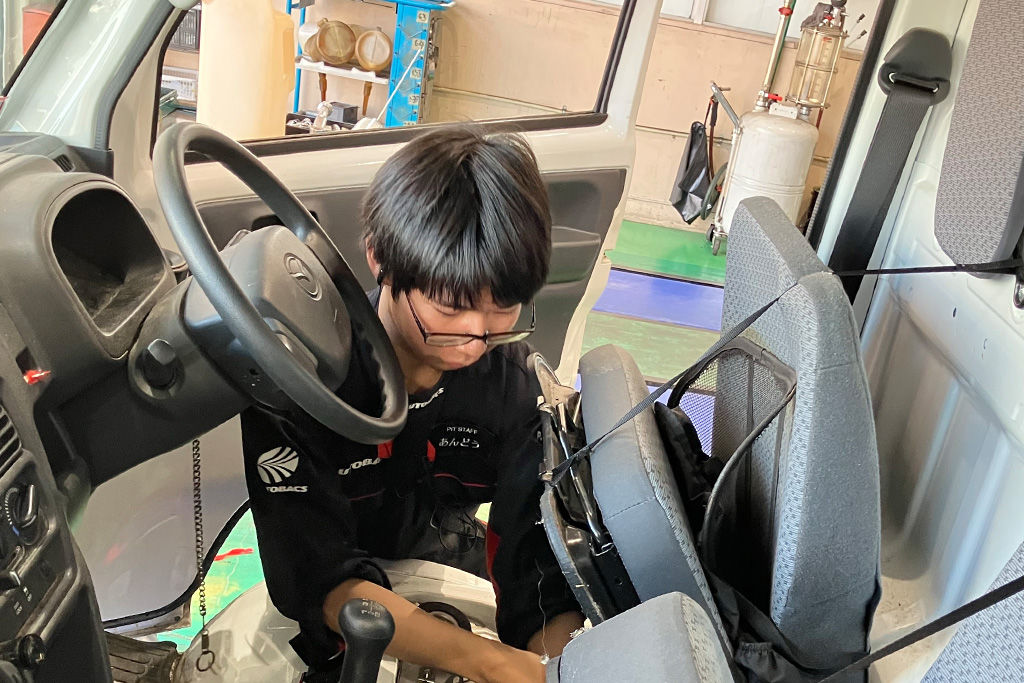 作業服を着た安藤宥人さんが、白い軽トラックの車内で身をかがめ点検作業をしている。