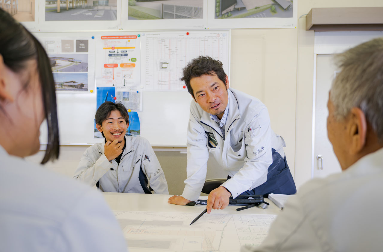 会議室で図面を広げて笑顔で先輩社員と打ち合わせを行う様子