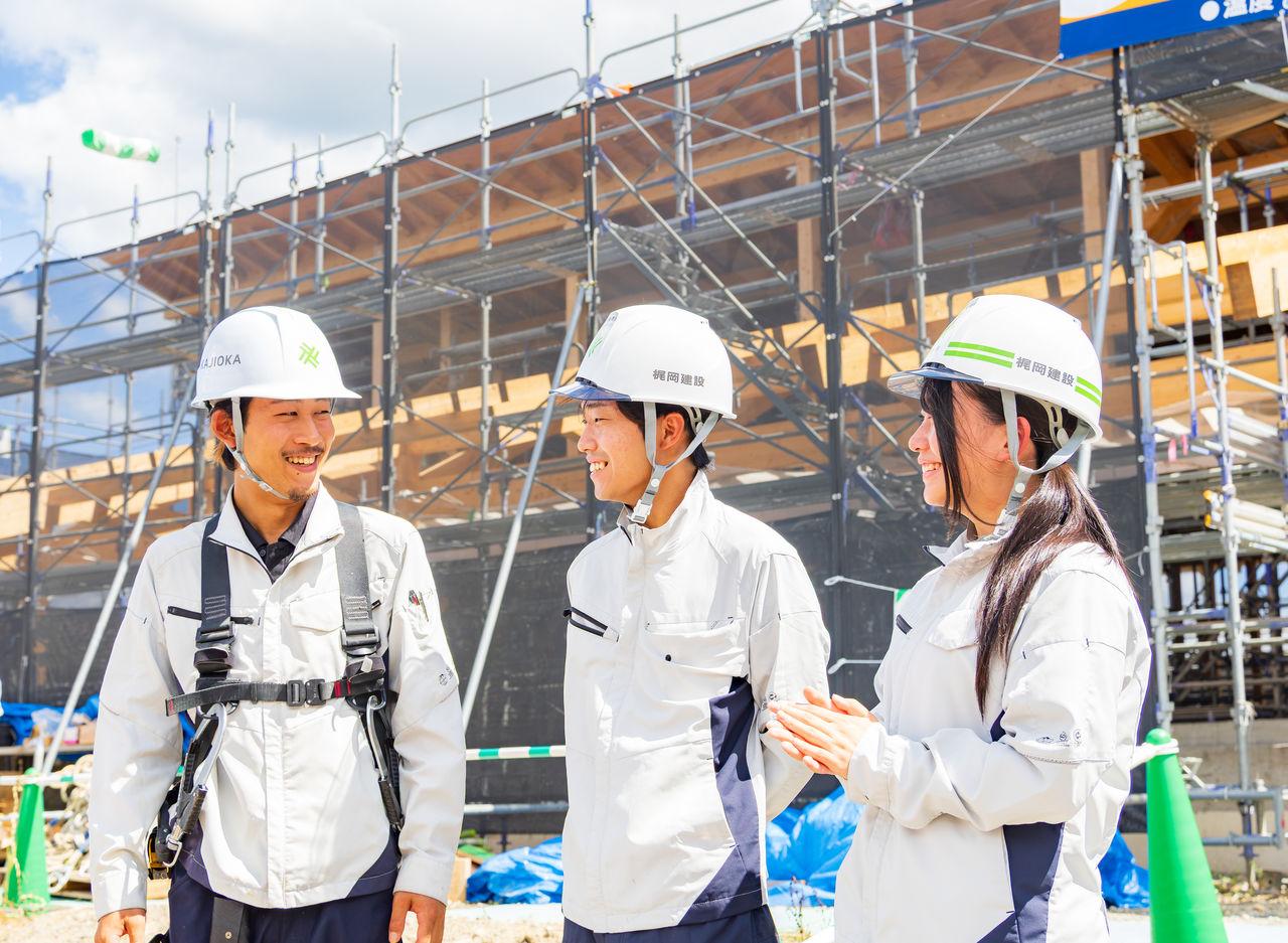 建築現場の前で笑顔で談笑するヘルメット姿の社員3名