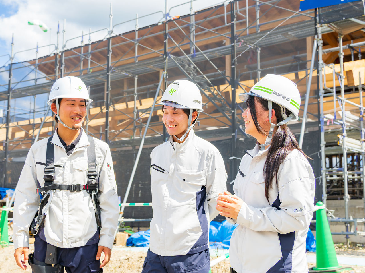 建築現場の前で笑顔で談笑するヘルメット姿の若手社員たち