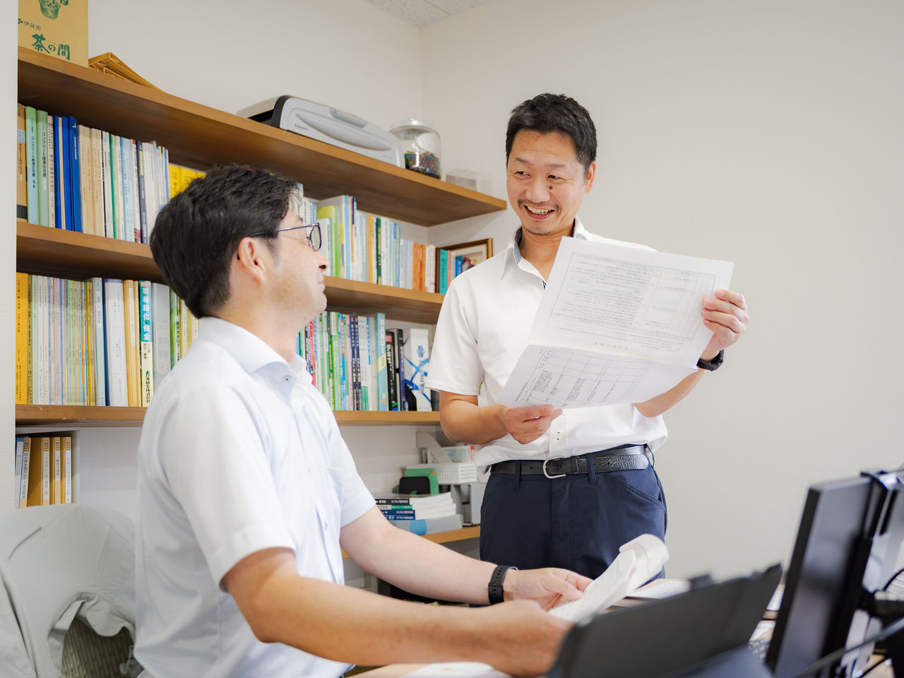 オフィスで書類を手に笑顔で業務の相談をする社員たち