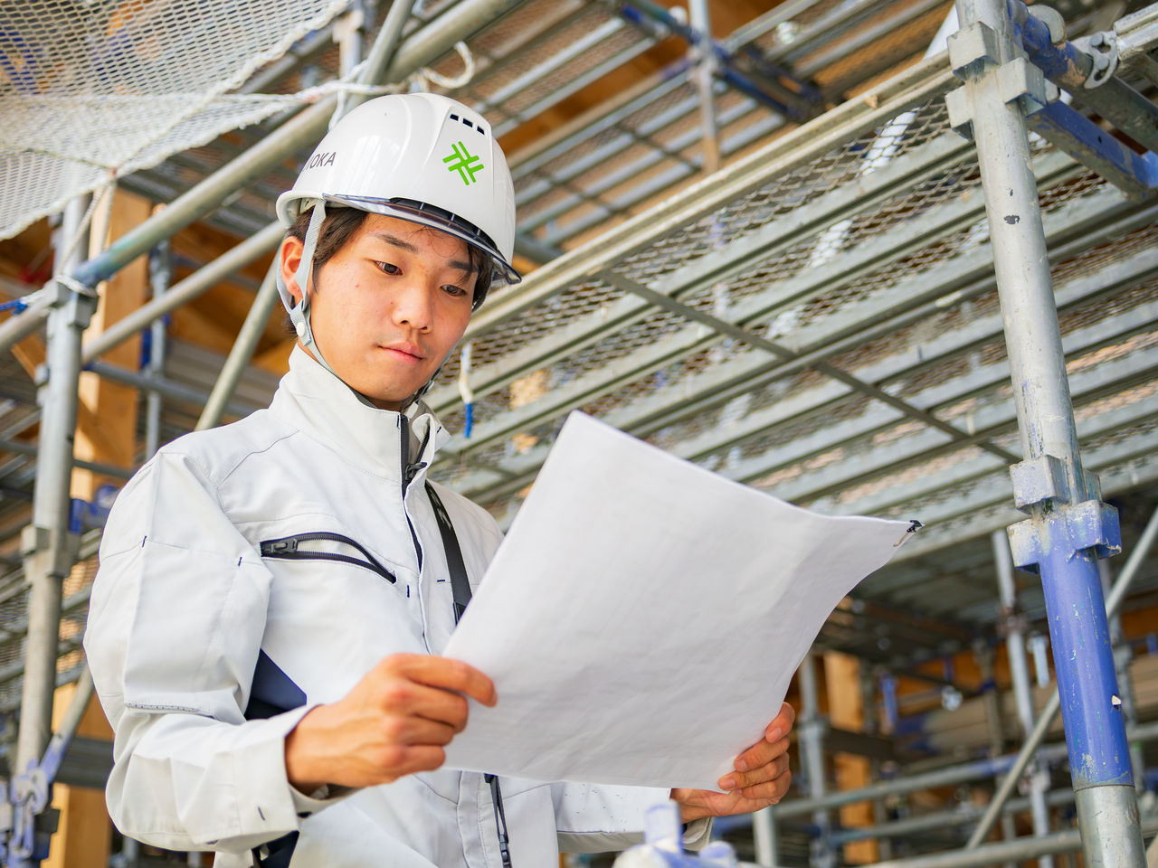 建築現場の足場内で図面を広げて真剣に見つめる施工管理者