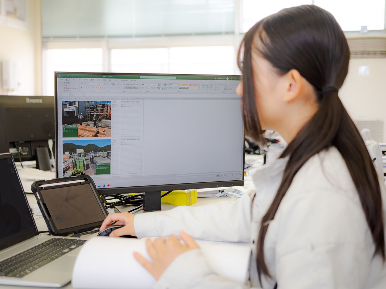 オフィスデスクでPC画面に向かい工事写真台帳を整理する女性スタッフ