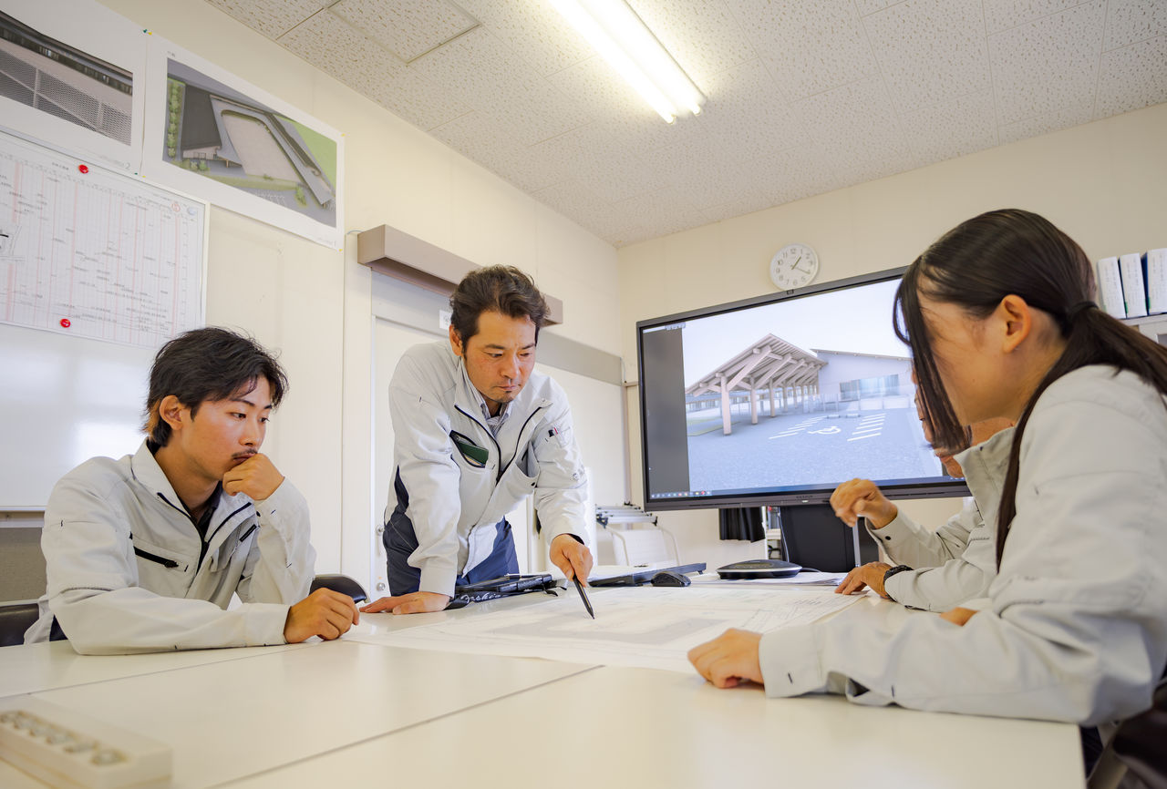 会議室で図面を囲みチームメンバーと真剣に打ち合わせを行う様子