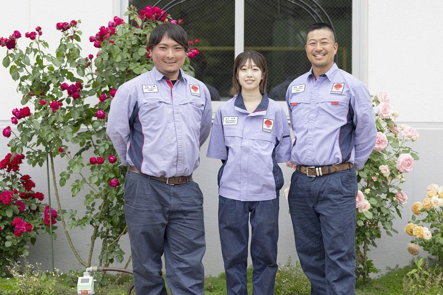 建物の外にあるバラの植え込みの前に並んで立つ3名の社員