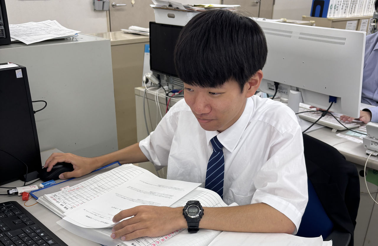 デスクでパソコンに向かい、書類を確認しながら仕事をする様子