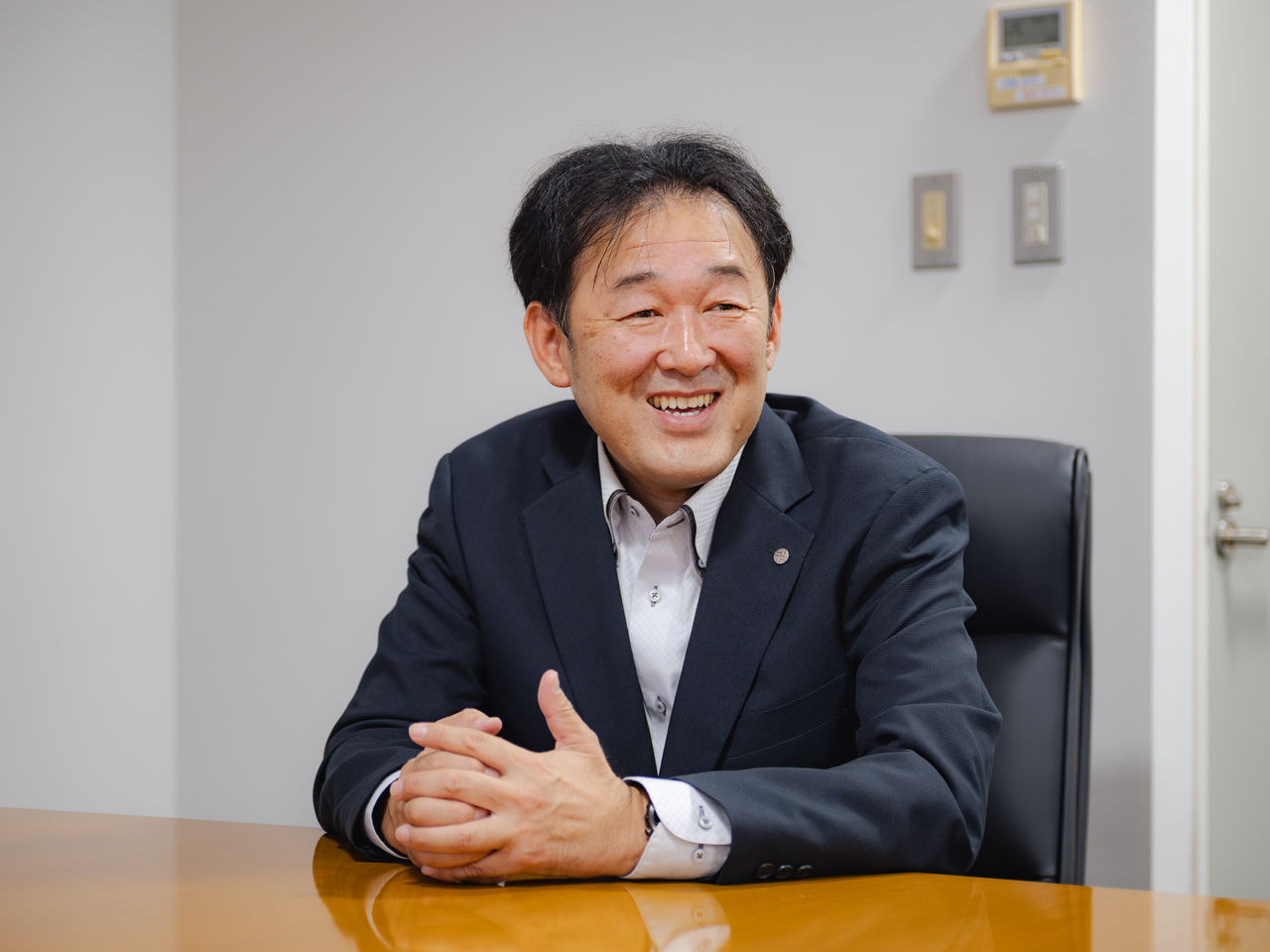 テーブル席で手を組み笑顔で話す梶岡秀成さん