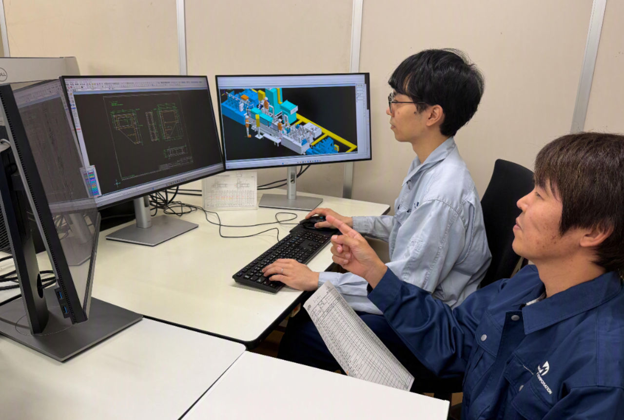パソコンのモニターを見ながら同僚と打ち合わせをする様子
