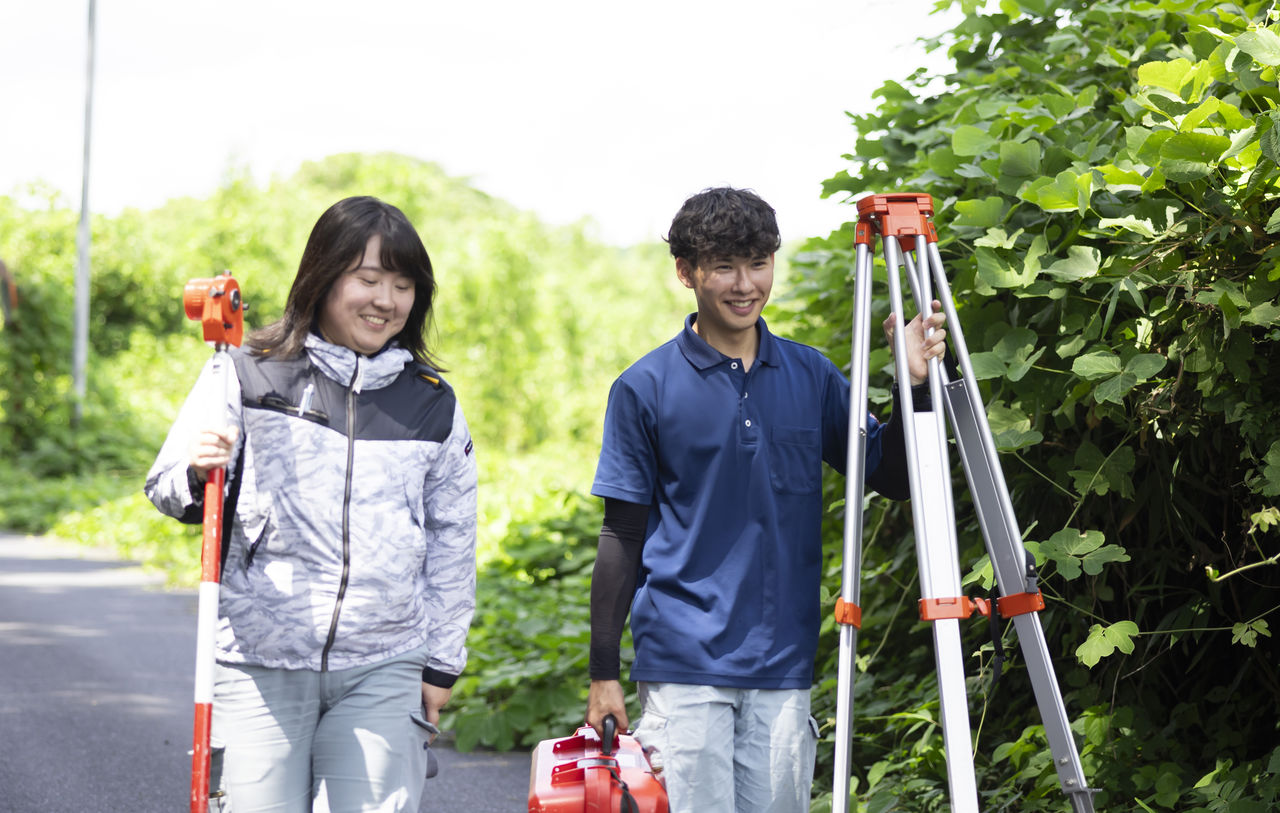 測量機器やポールを手に笑顔で並んで歩く貝阿弥明希さんと長嶋奈津美さん