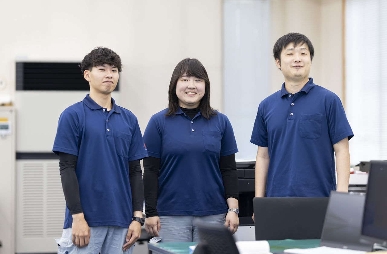 オフィス内で同僚たちと並んで笑顔を見せる杉山永治さん