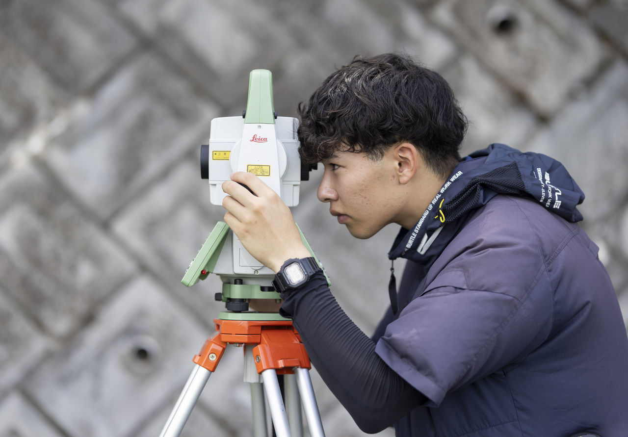 三脚に据えた測量機器を真剣な表情で覗き込む貝阿弥明希さん