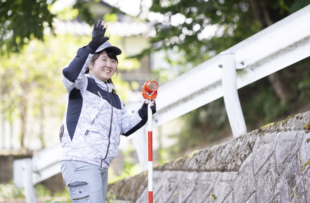 測量ポールを手に持ち笑顔で手を振って合図を送る長嶋奈津美さん
