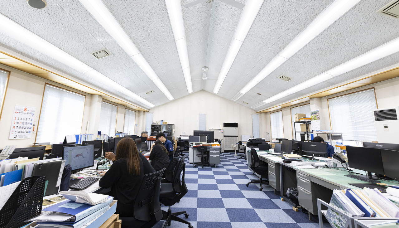 高い三角屋根と明るい照明が印象的なオフィスで業務に集中する社員たち