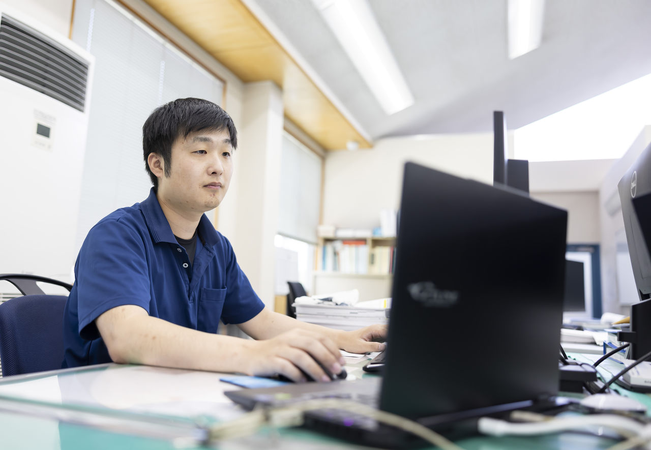 デスクでパソコンに向かい真剣な表情でマウスを操作する杉山永治さん