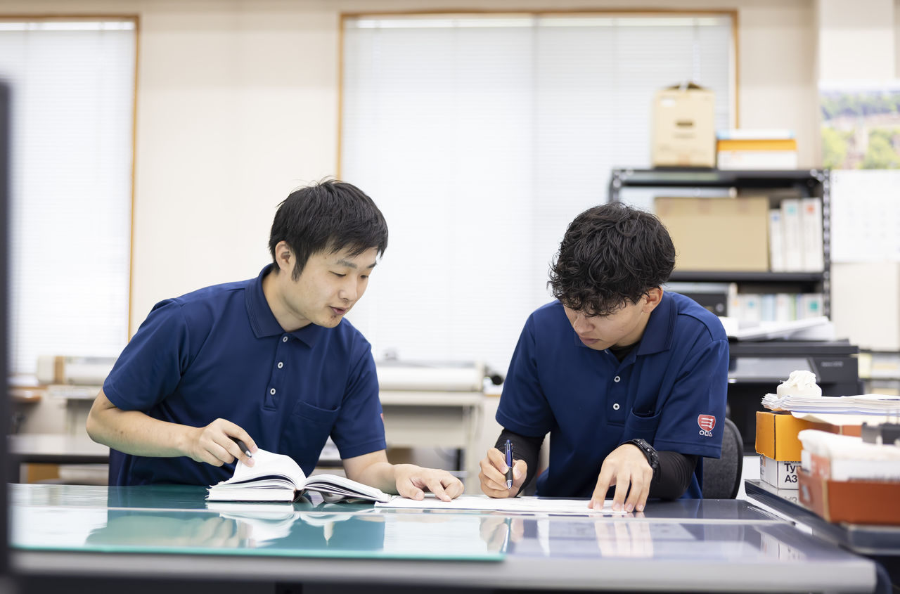 デスクで資料を広げ後輩社員と打ち合わせを行う杉山永治さん