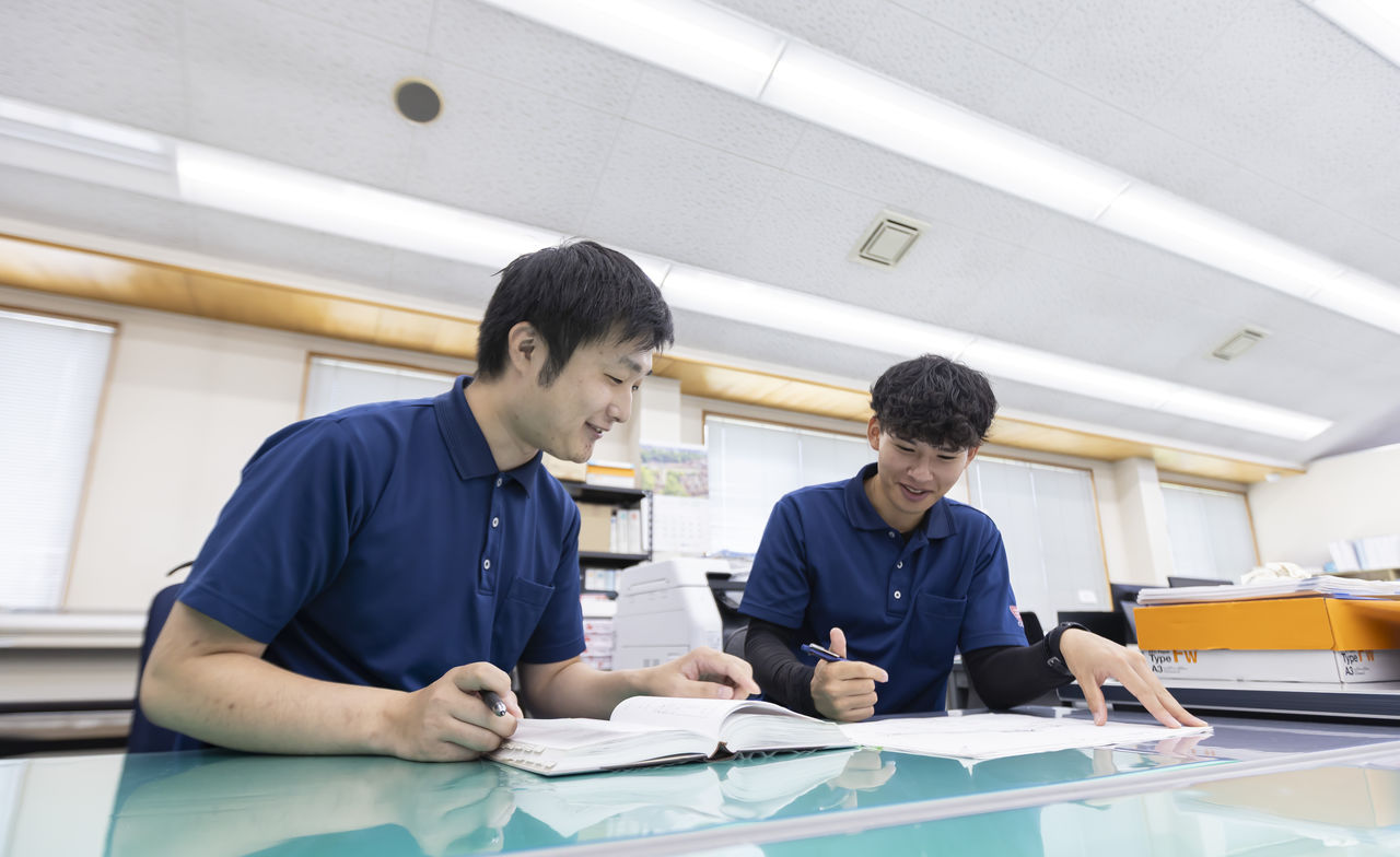 デスクで専門書を開きながら笑顔で相談し合う社員たち