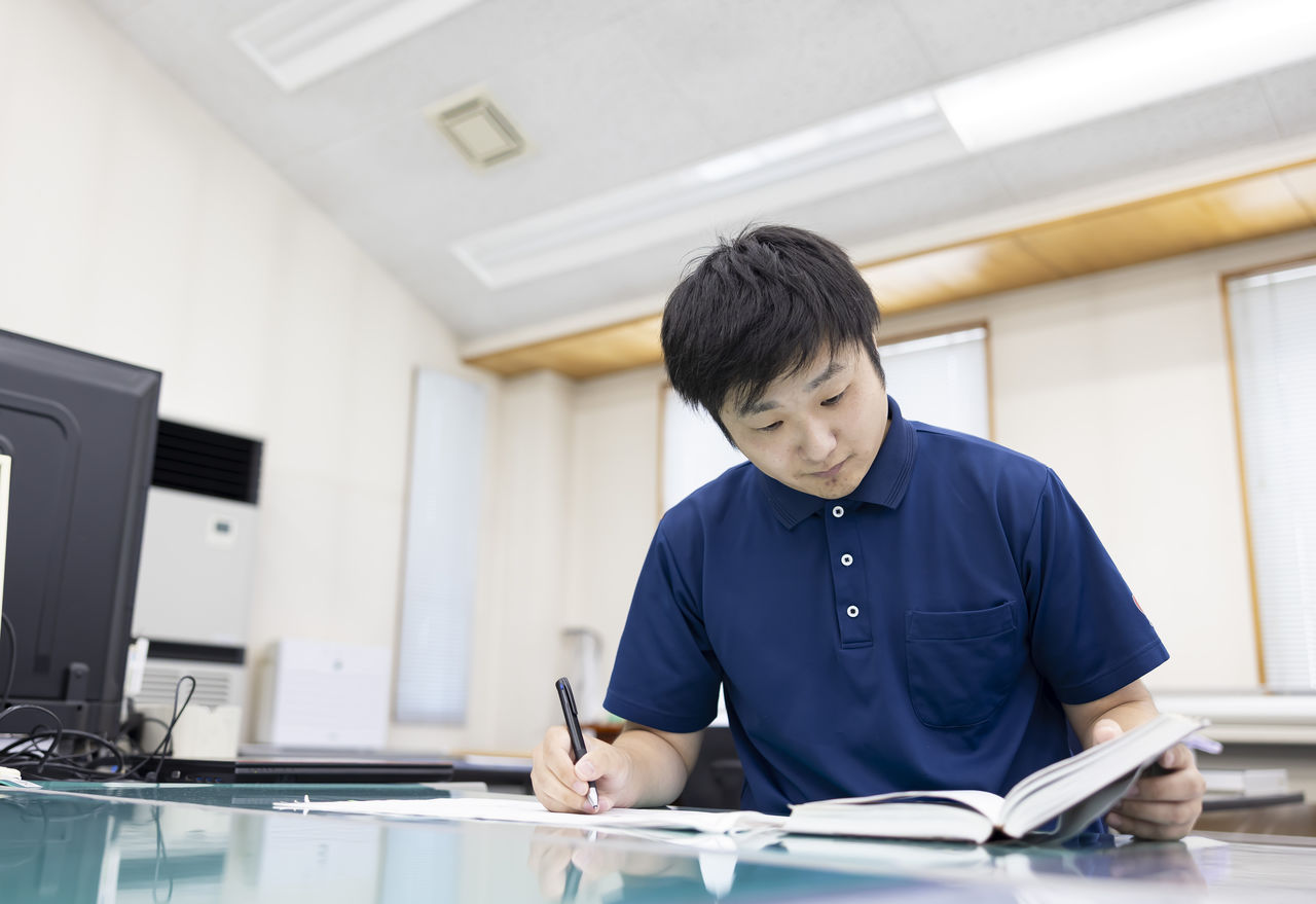 机で本を開きペンを握って資格取得の勉強に励む社員
