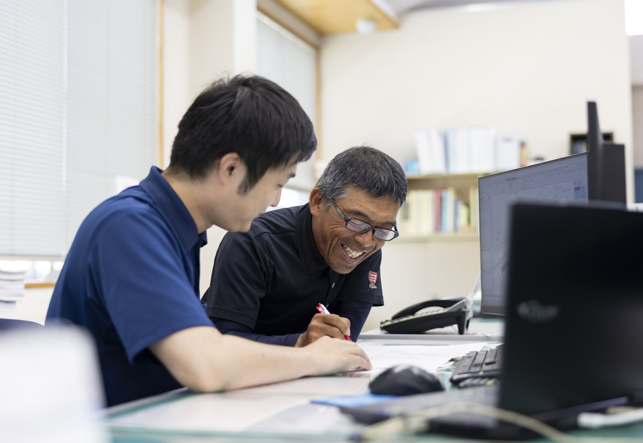 デスクで先輩社員から笑顔で親身な指導を受ける社員