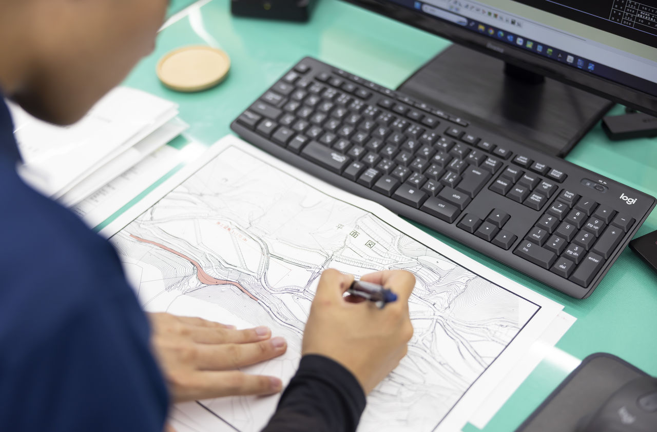 デスクに広げた地形図面にペンで書き込みを行い確認する社員の手元