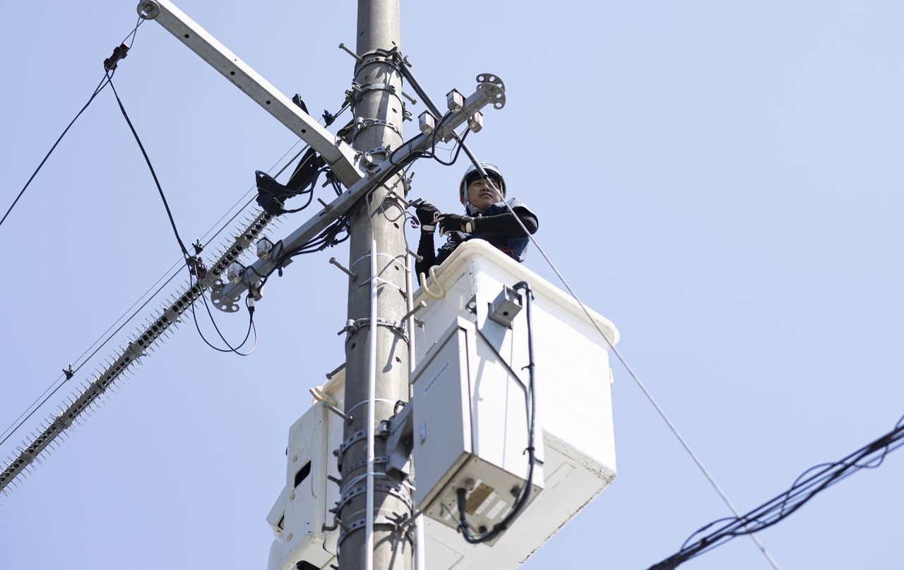青空を背景に高所作業車のバケットから電柱工事を行うスタッフ