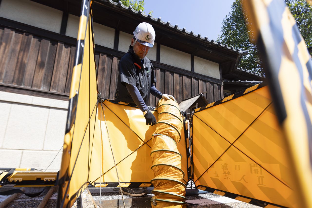 マンホールの安全柵の横で送風ダクトを扱う山本智弘さん