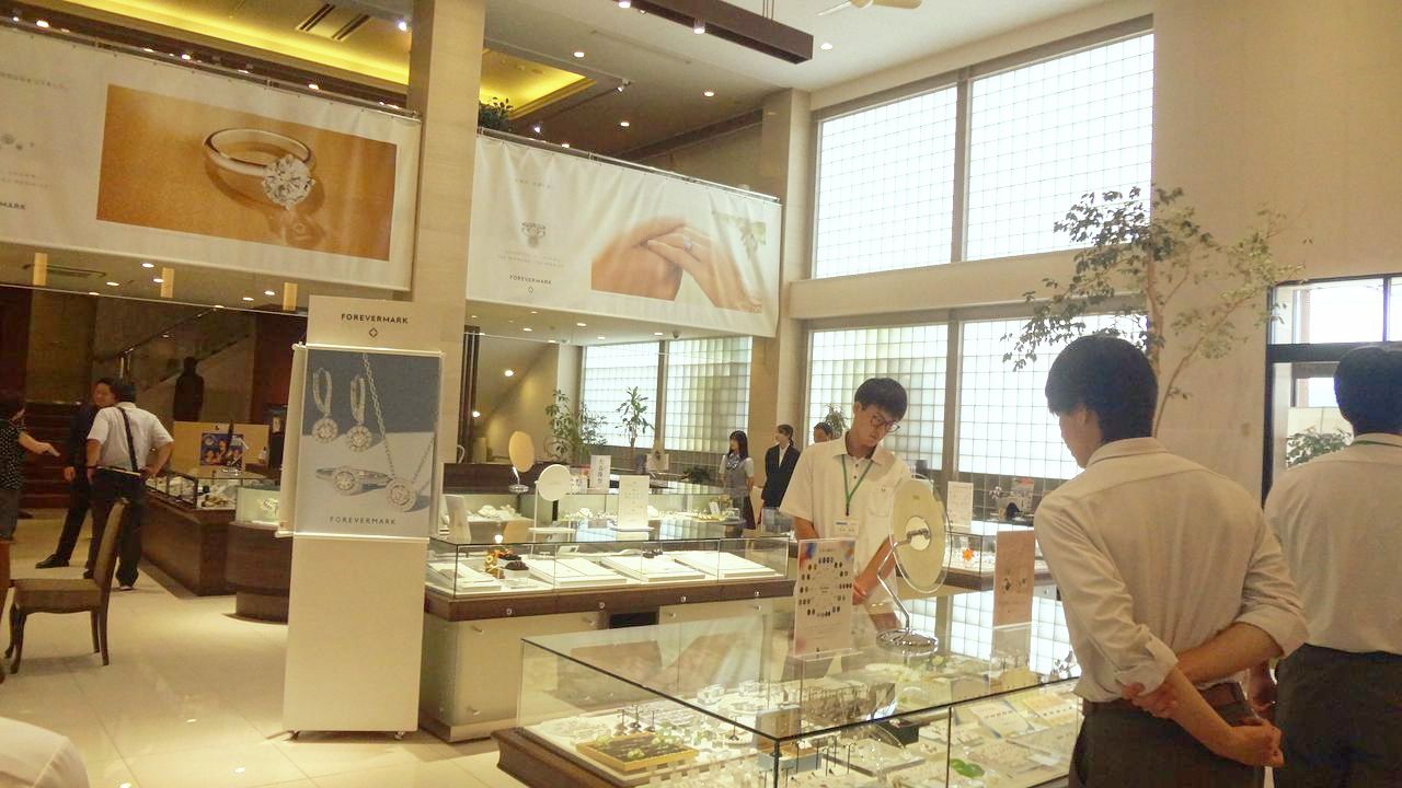 ジュエリーKANDA本店のショーケース前に並び店内の装飾品を見学する高校生たち